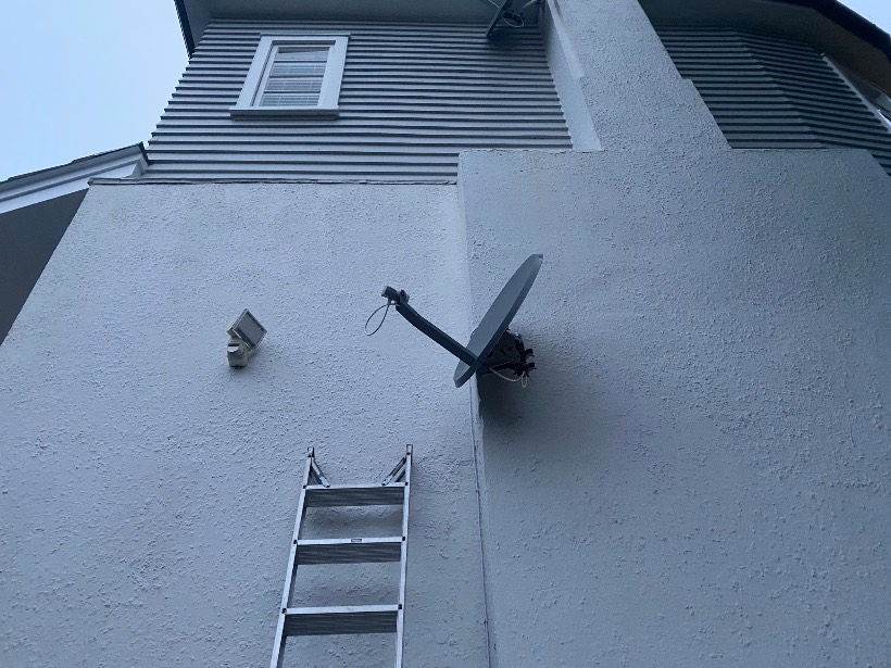 Technician diagnosing a satellite dish on a two-storey wall